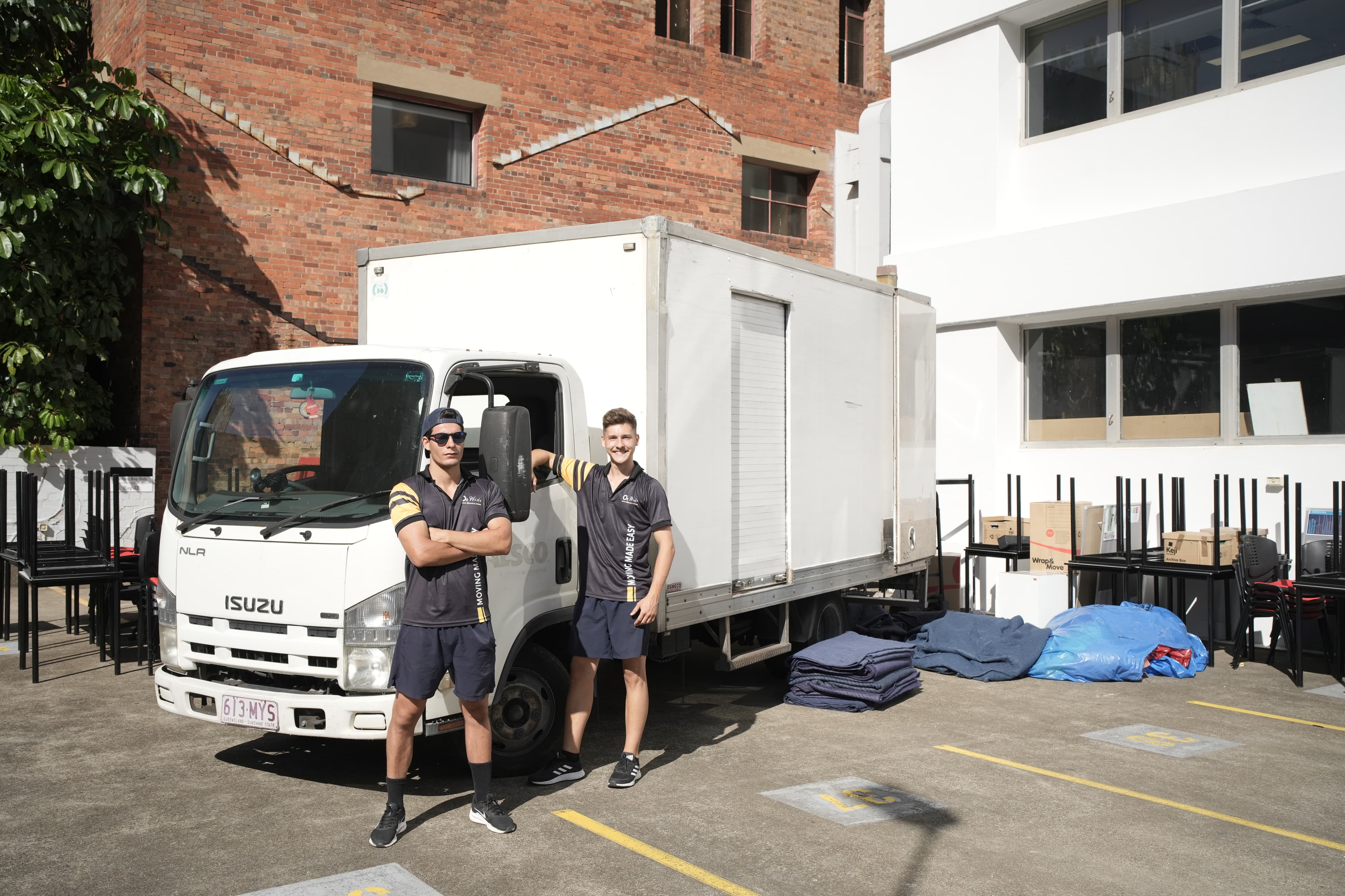 Two Oz Wide Movers in uniform beside a loaded removals truck